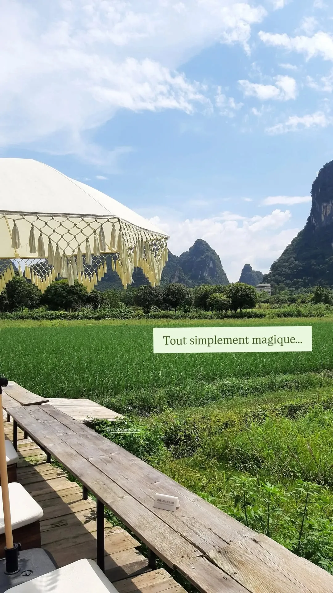 Bohemian Cafe Terrace Overlooking Yangshuo Rice Paddies Bohemian outdoor cafe bench with fringe umbrella overlooking green rice fields and limestone karst mountains in Yangshuo