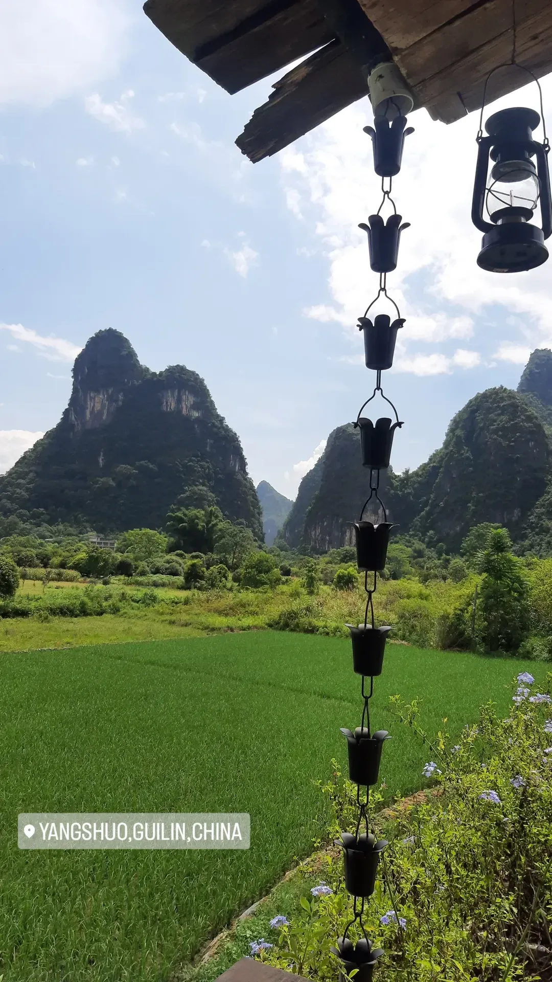 Scenic Countryside View of Yangshuo Karst Peaks with Rain Chain Panoramic countryside view of green rice fields and dramatic limestone karst peaks framed by a traditional rain chain in Yangshuo China