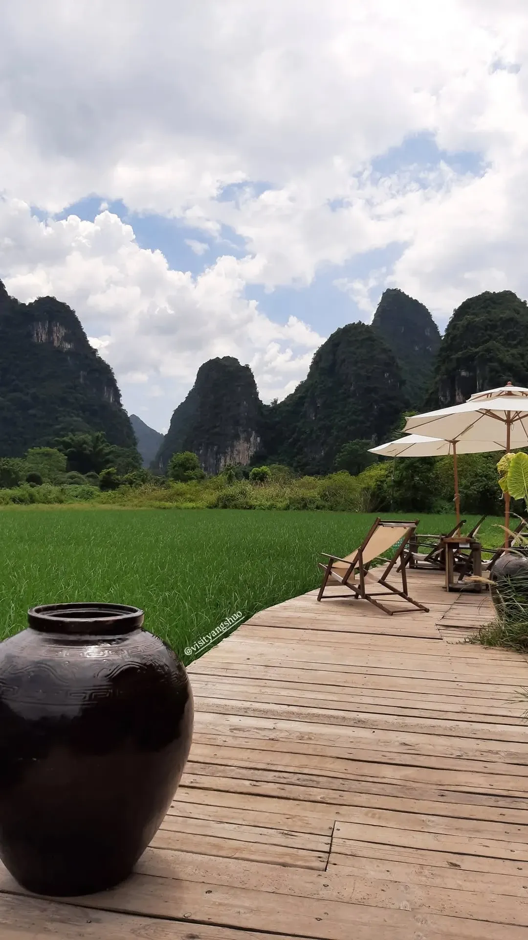 Wooden Terrace and Sun Loungers Overlooking Yangshuo Rice Fields Outdoor wooden deck with sun loungers and traditional ceramic jar overlooking green rice paddies and karst mountains
